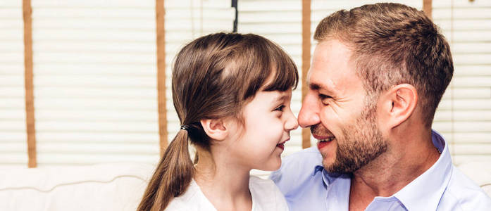 在家里，小女孩和爸爸一起微笑着抚摸鼻子。