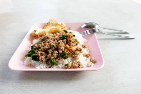 Rice topped with stirfried pork and basil in a white dish. 