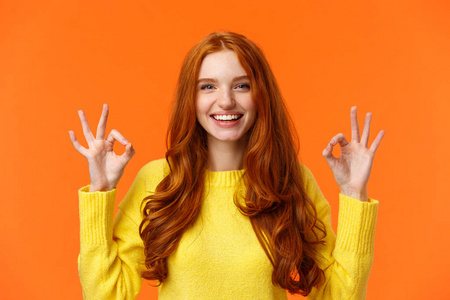 时尚购物寒假概念。迷人开朗的红发女人，有良好的手势和微笑，一切正常，认可或喜欢产品，推荐网上商店，橙色背景