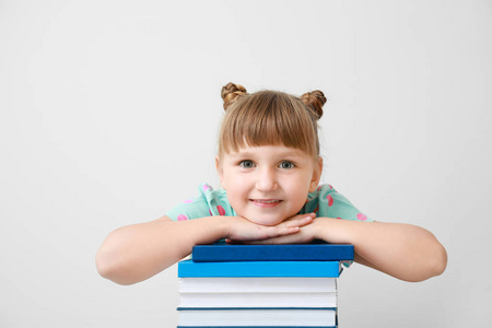 可爱的小女孩拿着书在浅色的背景上
