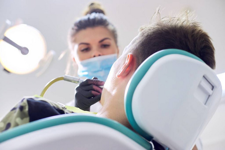 女牙医给病人治疗牙齿，年轻人在牙科诊所的椅子上