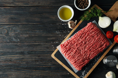 Spices and cutting board with minced meat on wooden background, 