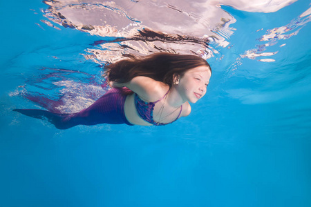 一个穿着美人鱼服装的女孩在水下游泳池里摆姿势.照片