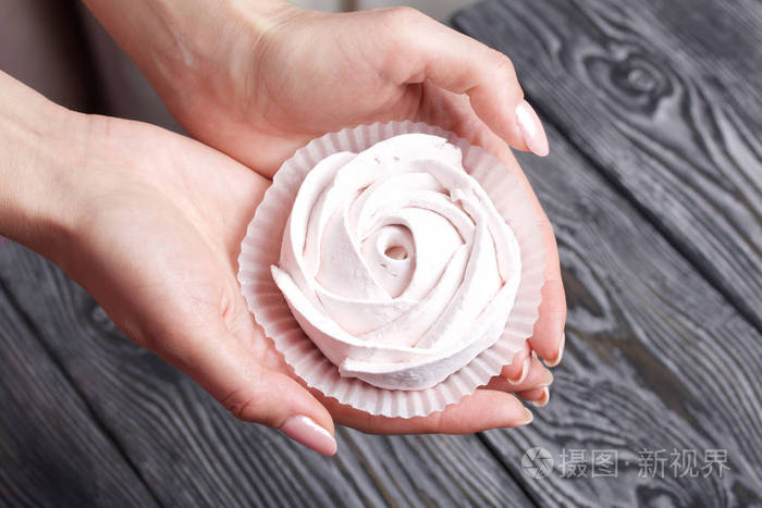 女人手掌中玫瑰状的棉花糖以黑白相间的拉丝松木板为背景