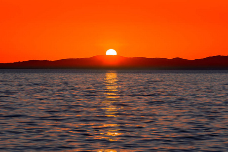 美丽的红色日落在海面上,阳光反射在水面和地平线上的山脉上,从