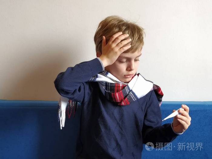 孩子沮丧地看着体温计,把手放在额头上,痛苦地忍受着