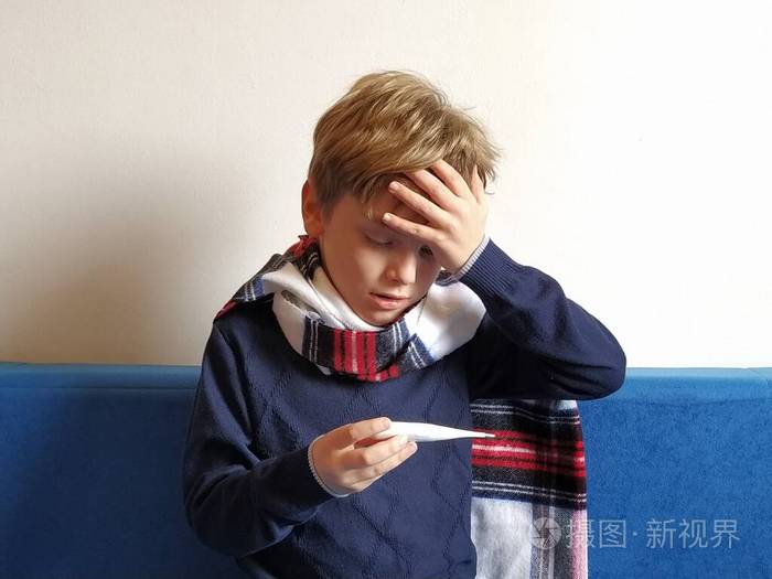 孩子沮丧地看着体温计,把手放在额头上,痛苦地忍受着