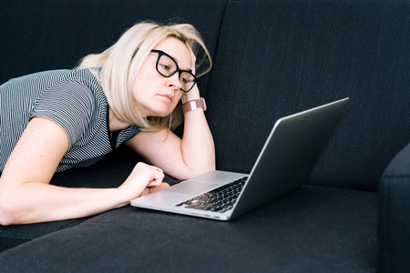 Casual woman with blond hair and eyeglasses lying on black sofa 