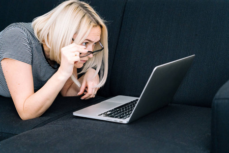 Casual woman with blond hair and eyeglasses lying on black sofa 