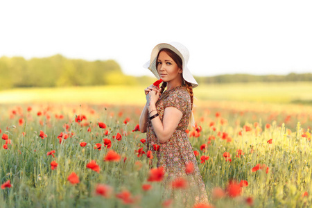 美丽的红发女人戴着帽子，在绿色的田野上开着花