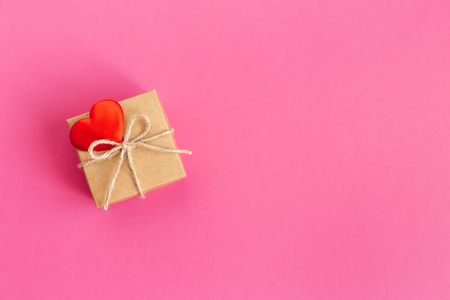 Craft gift box with red heart on a pink background. Holiday conc