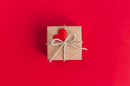 Craft gift box with red heart on a red background. Holiday conce