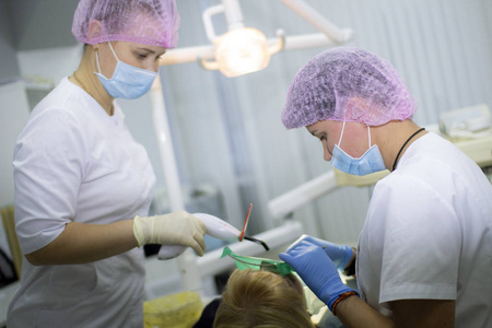一位女牙医和她的助手穿着白色制服给病人检查。医学，牙科。