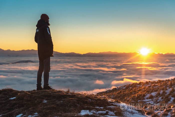 一个人站在山上日落时云端之上