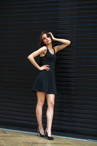深色皮肤的年轻女子，穿着性感的黑色连衣裙，室内工作室墙壁