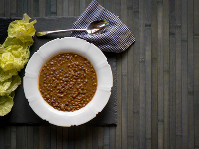 Lentils on a white plate, lettuce with oil, spoon and checkered 