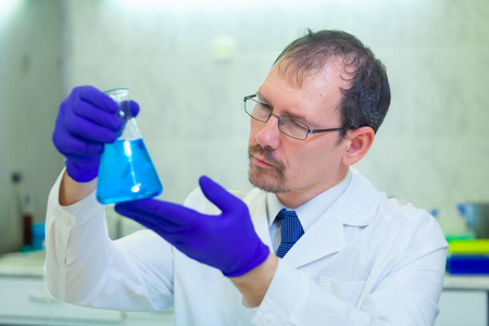科学家在科学实验室里拿着一个装有蓝色液体的烧瓶研究