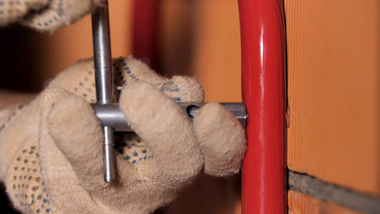 在套筒一名男工人用套筒扳手将金属管固定在红砖墙上的特写镜头.