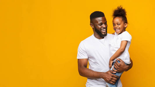 快乐的非洲男人在黄色背景上抱着小女儿