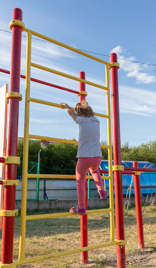 一个小孩子在体育场里参加体育运动挂在单杠上高低杠上