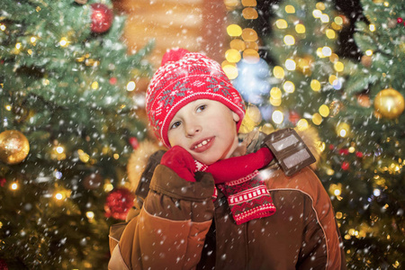圣诞背景下的宝贝。圣诞街上一个戴着红帽子的男孩。