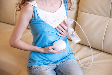 一位年轻的母亲手里拿着吸奶器坐在沙发上.照片
