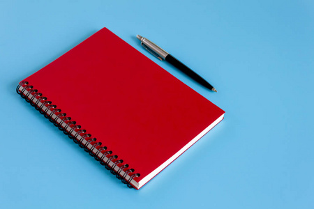 蓝色背景的红色笔记本和钢笔，学习和商务概念