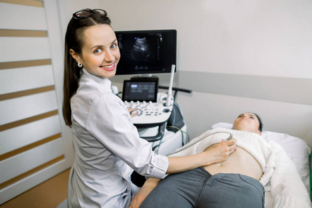 年轻笑脸女医生在医院对女性患者腹部进行超声检查时使用超声波机