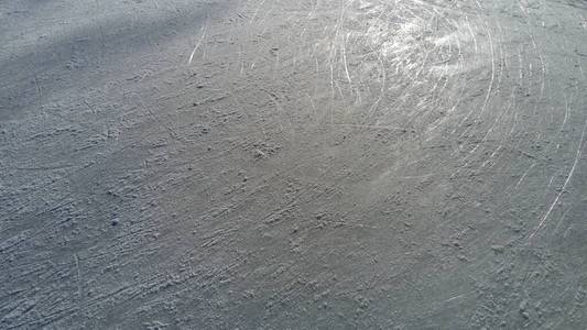 冰上有花样滑冰鞋尖的条纹。花样滑冰。滑冰运动员运动后的冰场表面。阳光洒在潮湿的春冰上。雪和冰水