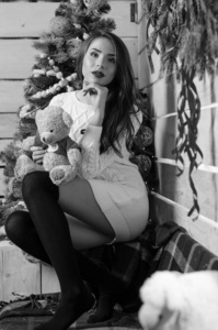 美丽性感的女人和背景圣诞树坐在优雅的椅子上，在舒适的风景。一个女孩的画像，摆着很短的紧身白色连衣裙。迷人的黑发女性，室内拍摄。