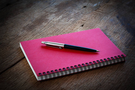 红色的笔记本和钢笔放在木制桌子上，以质感为背景，学习概念。