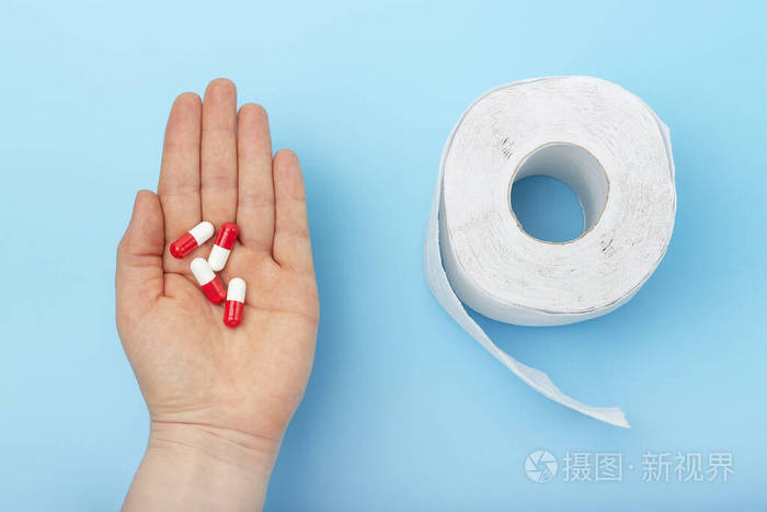 女性手拿着药片和蓝色背景的卫生纸一种腹泻或便秘的概念