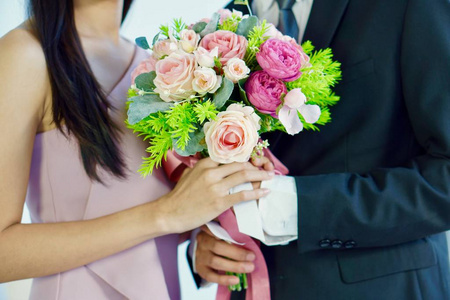 的女人和一个穿黑色西装的男人手里拿着一束粉红色的人造玫瑰花照片