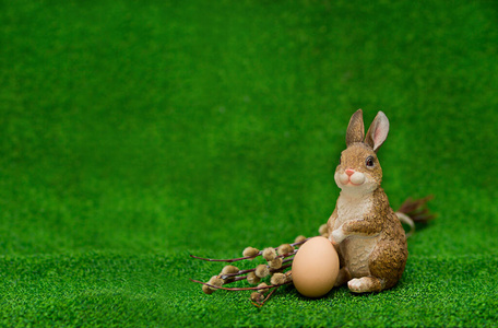 复活节兔子坐在草地上,拿着一根柳枝和一个鸡蛋,在右边的一个绿色背景