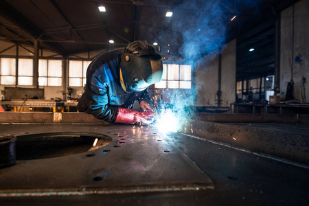 金属加工厂焊接金属零件的专业工业焊工。戴防护面罩和手套的工人。闪光和火花飞溅。