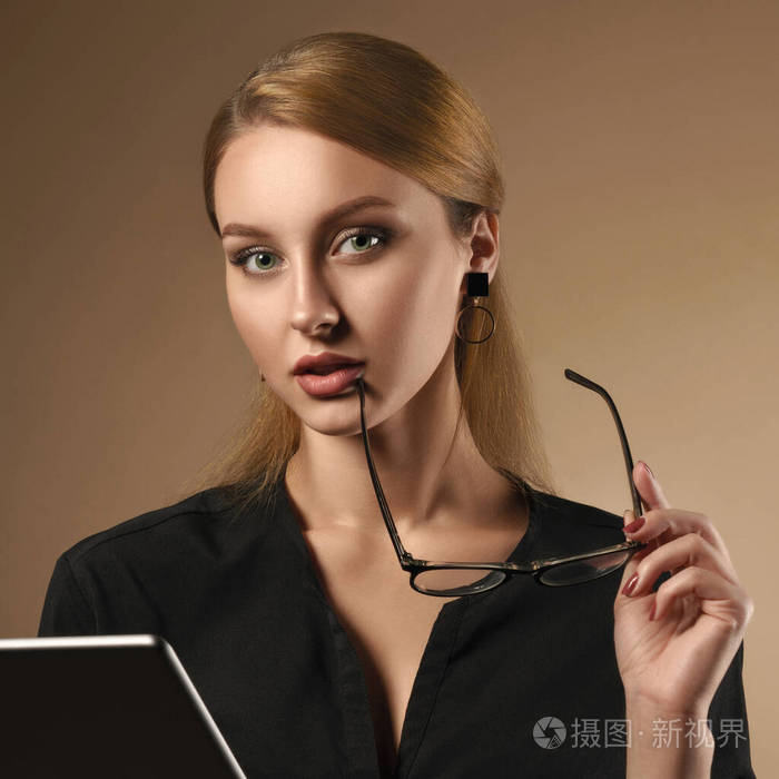 身穿黑色衬衫的女孩在使用米色背景的平板电脑时摘下眼镜