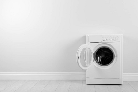 Modern washing machine near white wall, space for text. Laundry 
