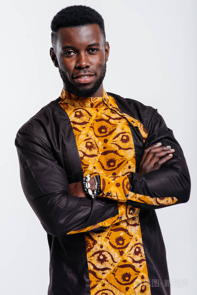 在白色背景下穿着黄黑色传统服装双手交叉直视镜头的美国黑人男性的
