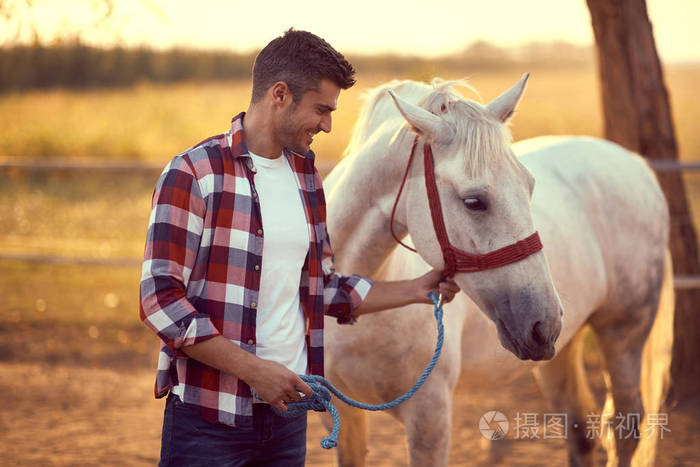 英俊微笑的男人牵着他的白马countrysid的乐趣