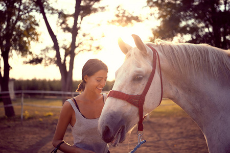 Smiling woman pets her white horse. fun on countryside,  golden 