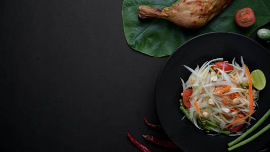 Top view of papaya salad on black plate, chicken grill on green 