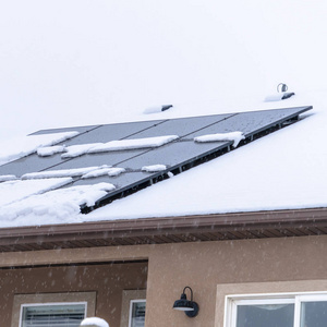 方形框架的雪落在家里冰冷的屋顶上，用太阳能板顶住多云的天空