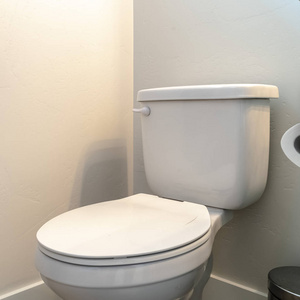 图为垃圾桶旁的方形厕所和带纸巾架的浴室柜