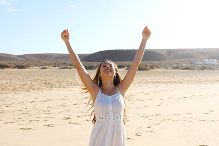 清晨,快乐的年轻女子在沙滩上高举双手享受自由照片