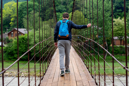 男子背包旅行，走在山村的吊桥上