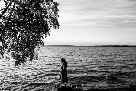 美丽苗条的女人穿着长裙在湖边散步。