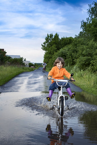 雨天在公园里骑自行车穿过水坑。双腿上的男孩