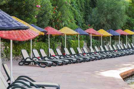 Empty sunbeds with colored umbrellas are in a row near the sea. 