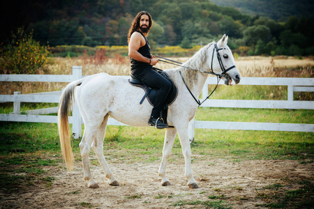秋天牧场上坐在白马上的漂亮男人.坐在他那英俊的小伙子旁边.照片