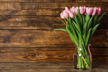 Beautiful pink spring tulips in vase on wooden table. Space for 